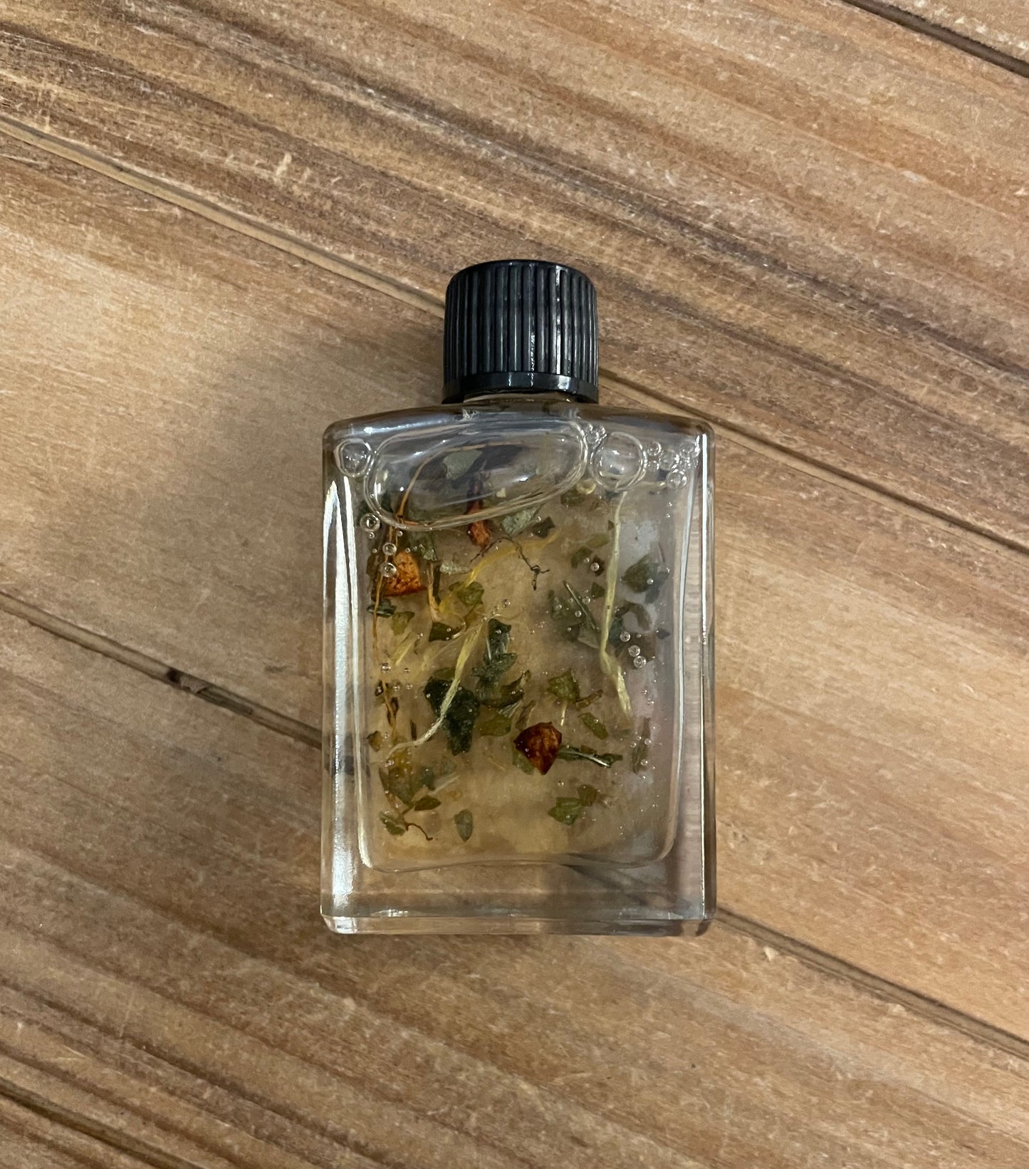 Small glass bottle with black cap containing dried herbs on a wooden surface