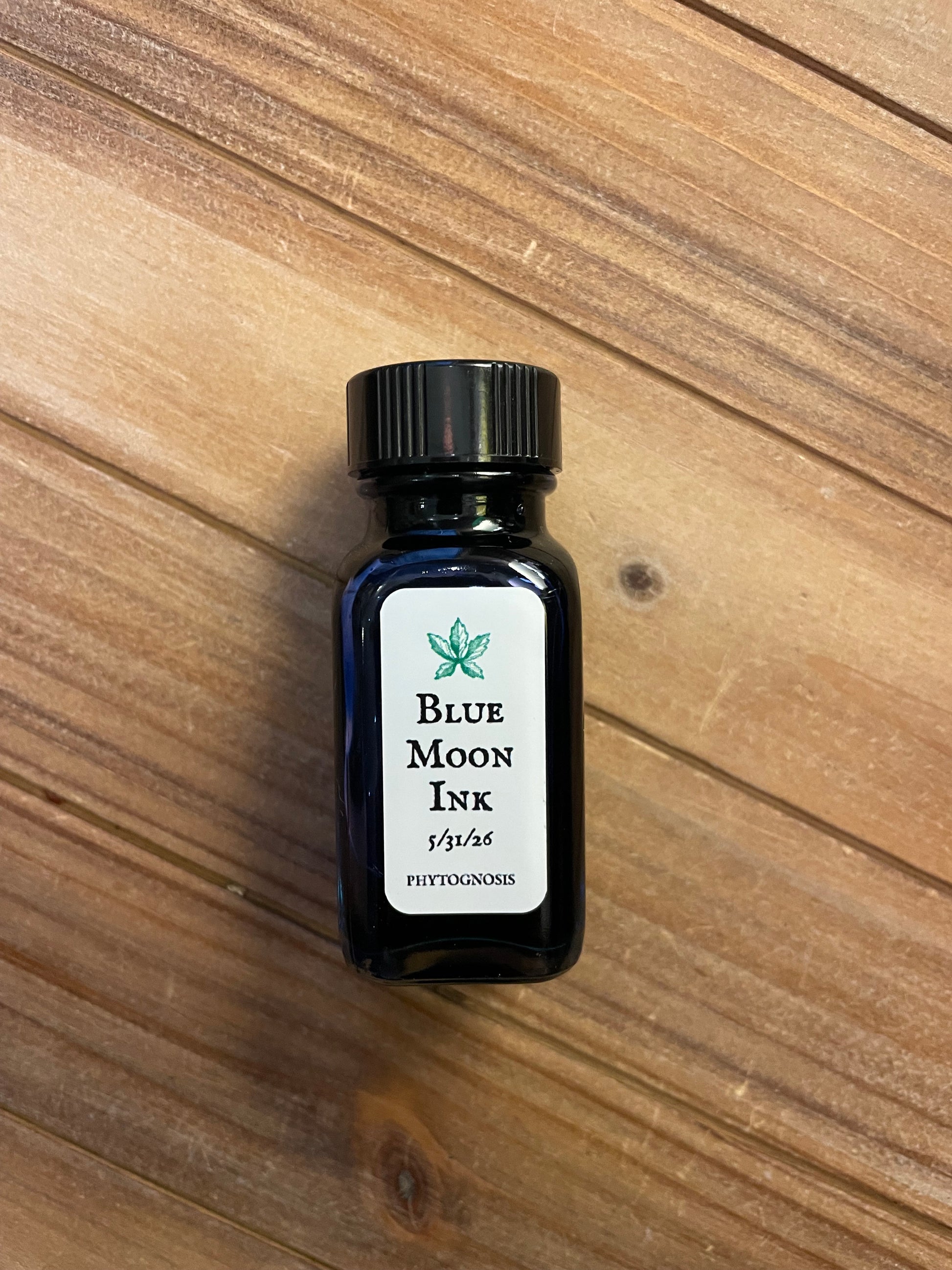 Small dark glass bottle of deep blue ritual ink, photographed on a wooden surface.