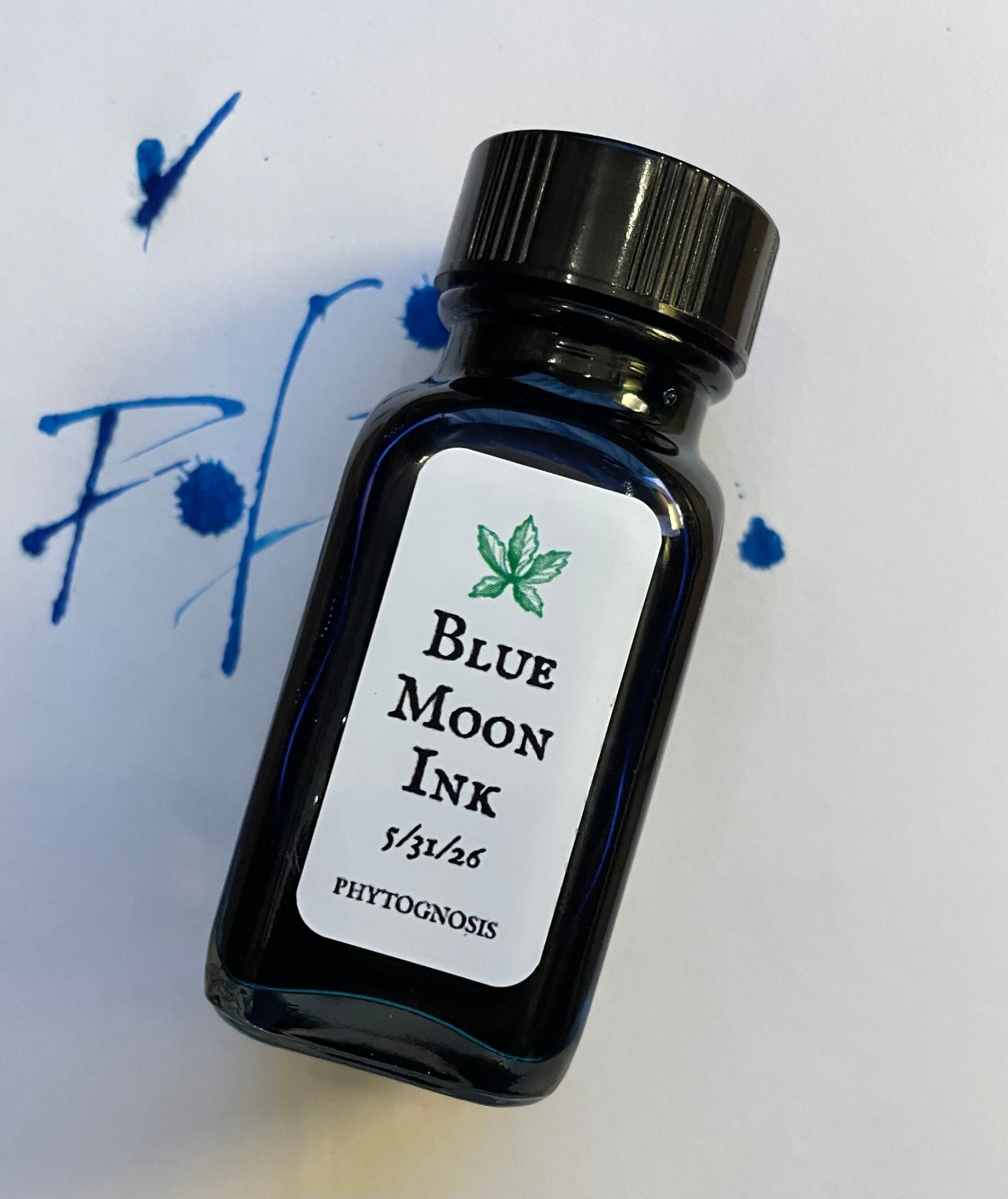 Small dark glass bottle of deep blue ritual ink with a label, photographed on a white surface.