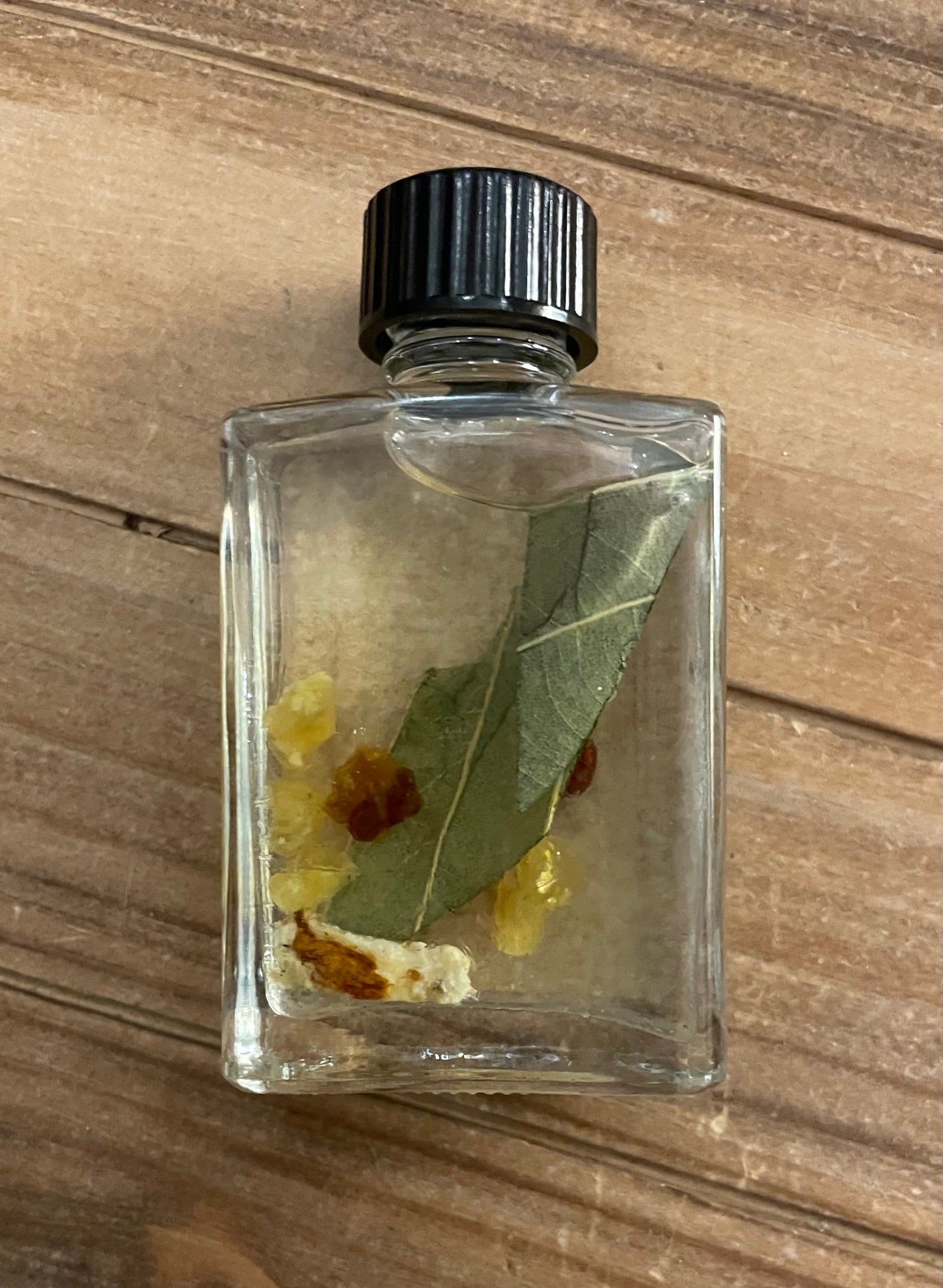 Small glass bottle with a black cap containing leaves and possibly insects on a wooden surface