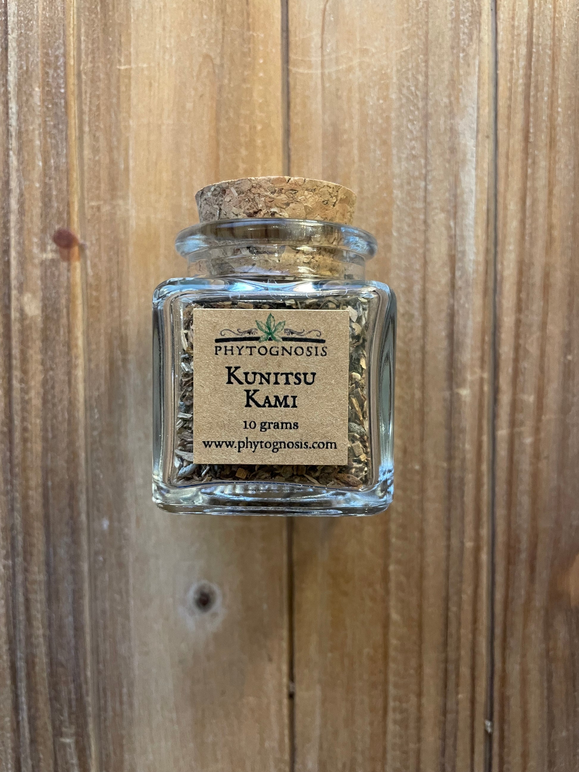 A small clear glass jar with a cork stopper and a beige label reading 'Phytognostic KuntiSU Kami 10 grams', placed on a wooden surface.