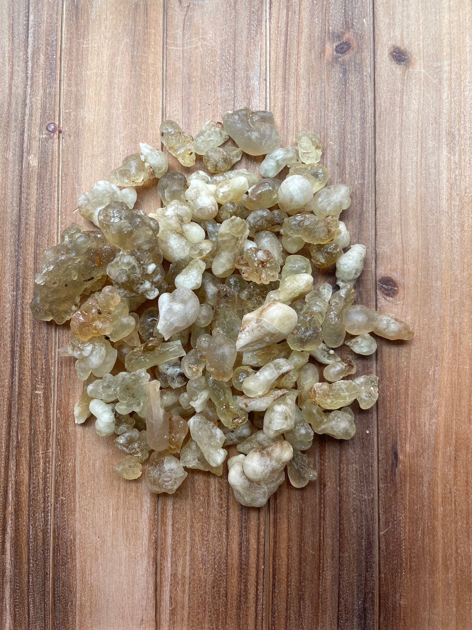 A pile of raw, unpolished translucent amber and pale greenish-brown resin stones or chunks, displayed on a rustic wooden surface.