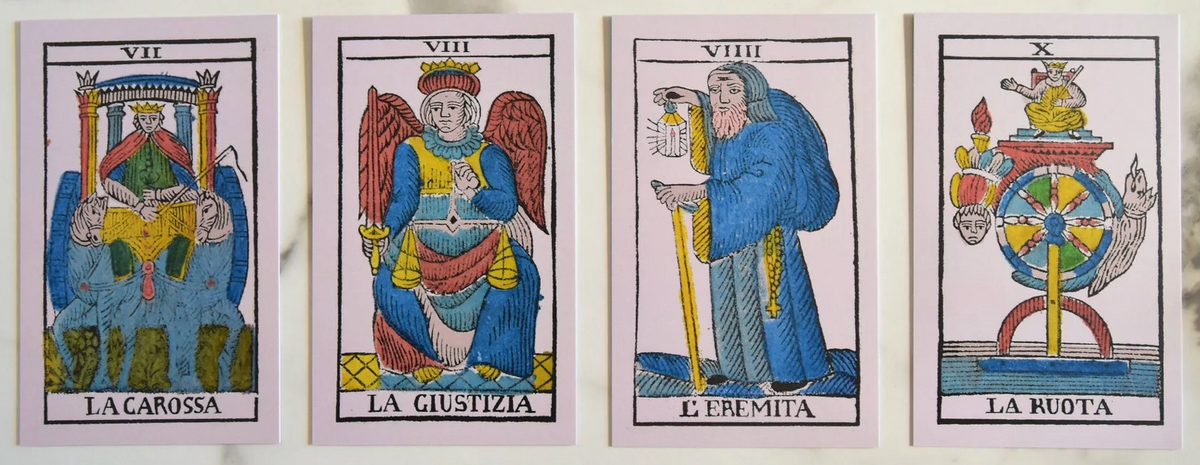 Four  tarot cards arranged side by side on a light surface, featuring traditional woodcut-style illustrations and Italian card titles: La Carossa, La Giustizia, L'Eremita, and La Ruota.
