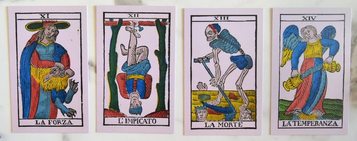 Four tarot cards laid out side-by-side on a light marble surface, featuring classic Renaissance-style illustrations with Spanish titles: La Forza, L'Impicato, La Morte, and La Temperanza.